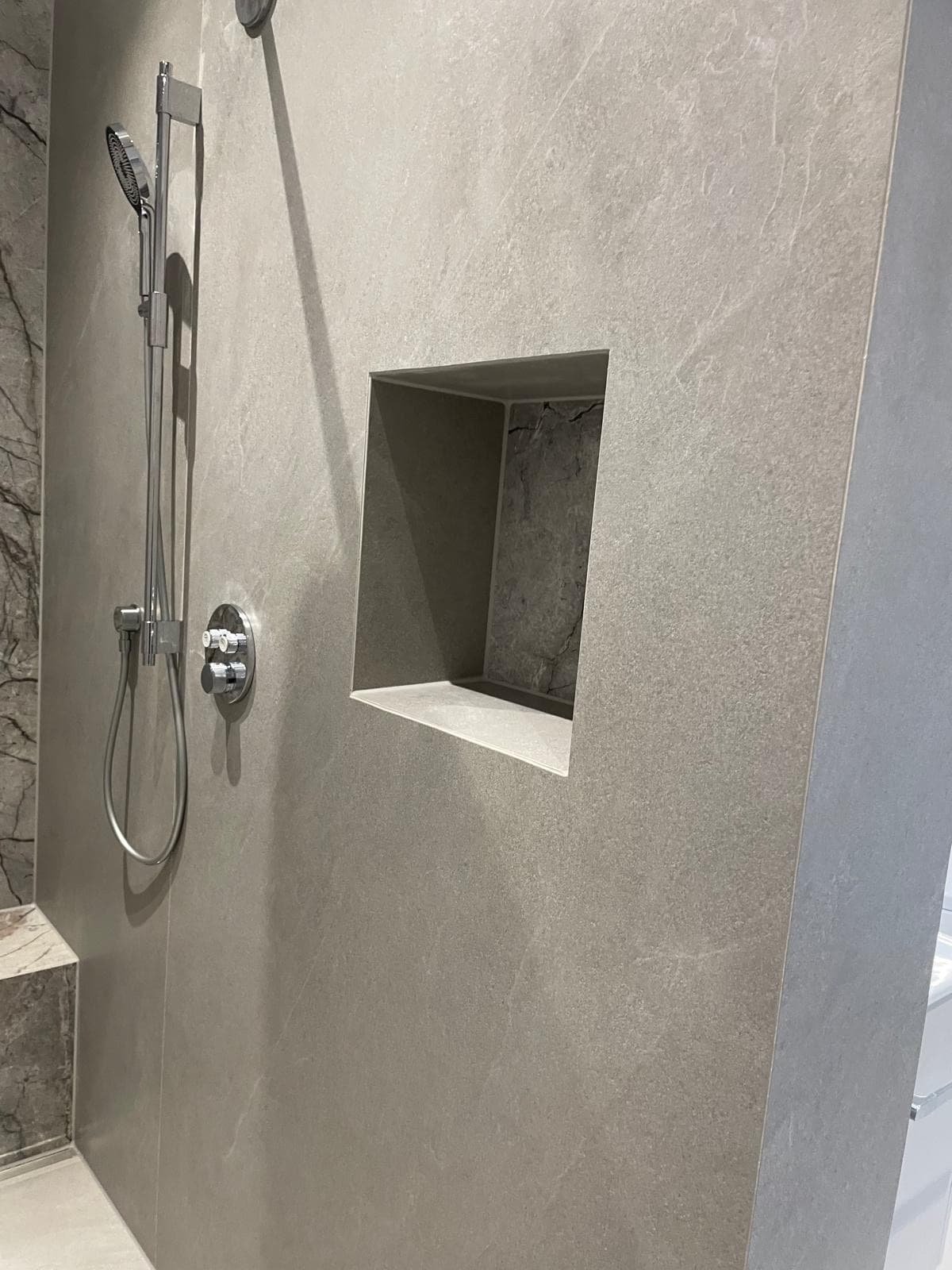 Dusche in grauer Marmoroptik mit Wandnische und Brausestange