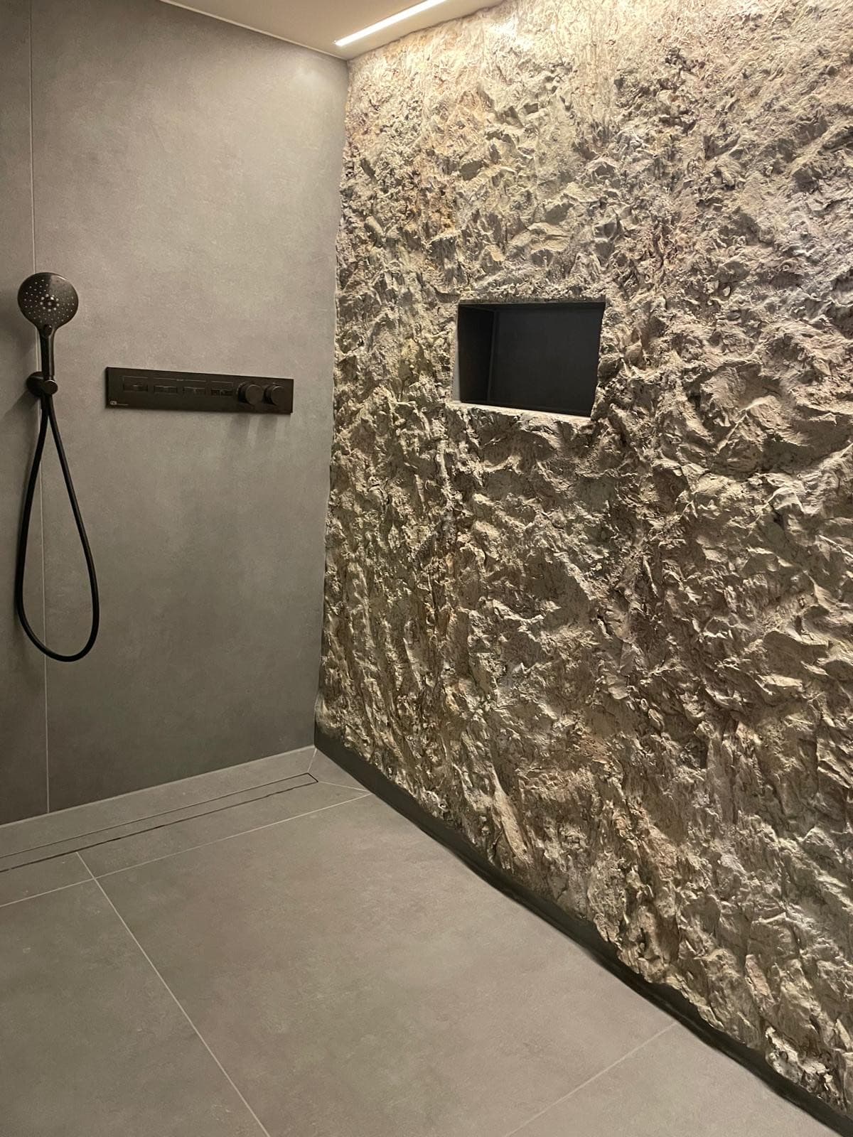 Dusche mit Spaltstein-Wand und schwarzer Armatur