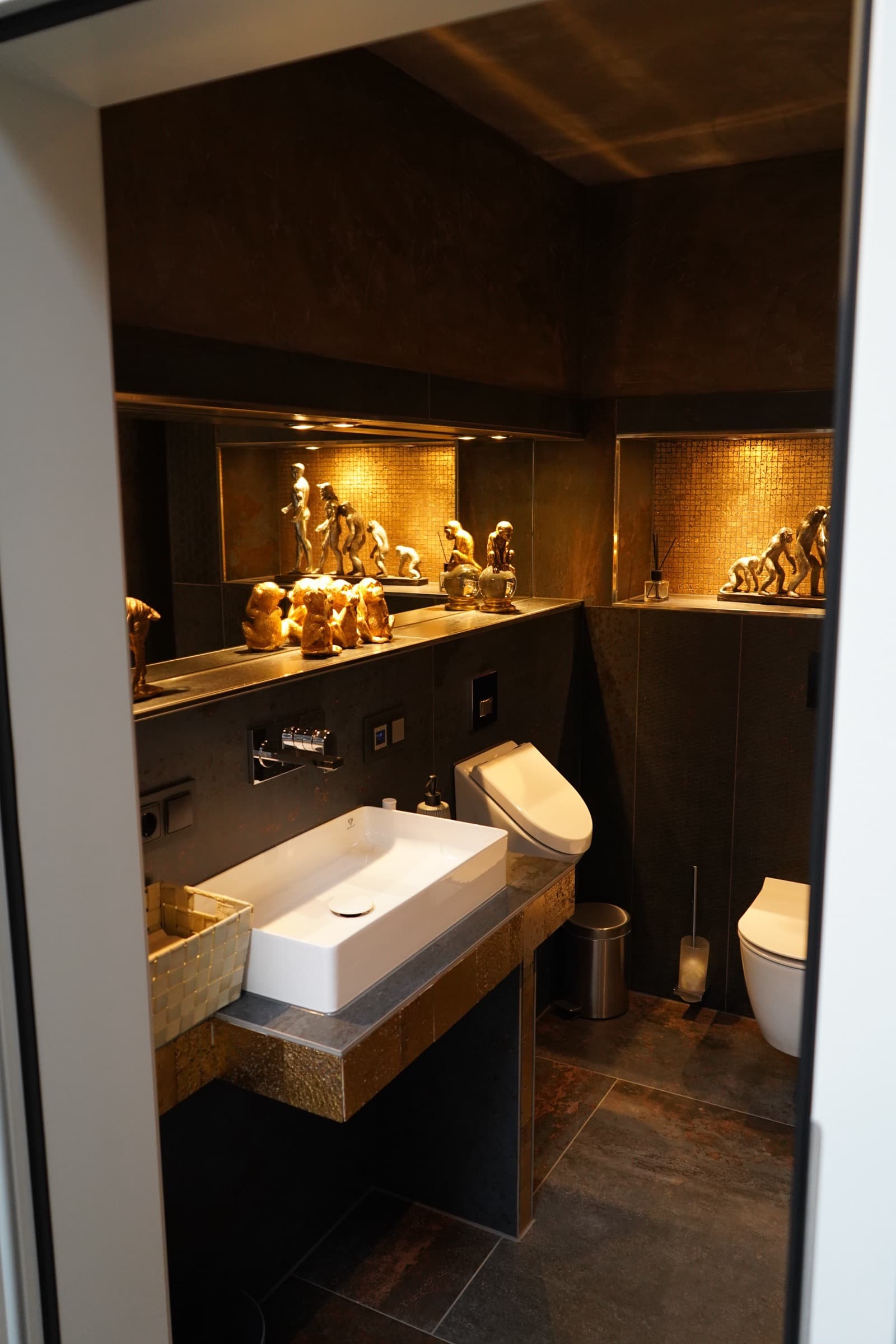 Gäste-WC der Ausstellung mit Goldmosaik in beleuchteten Nischen und dunklen Metallic-Fliesen