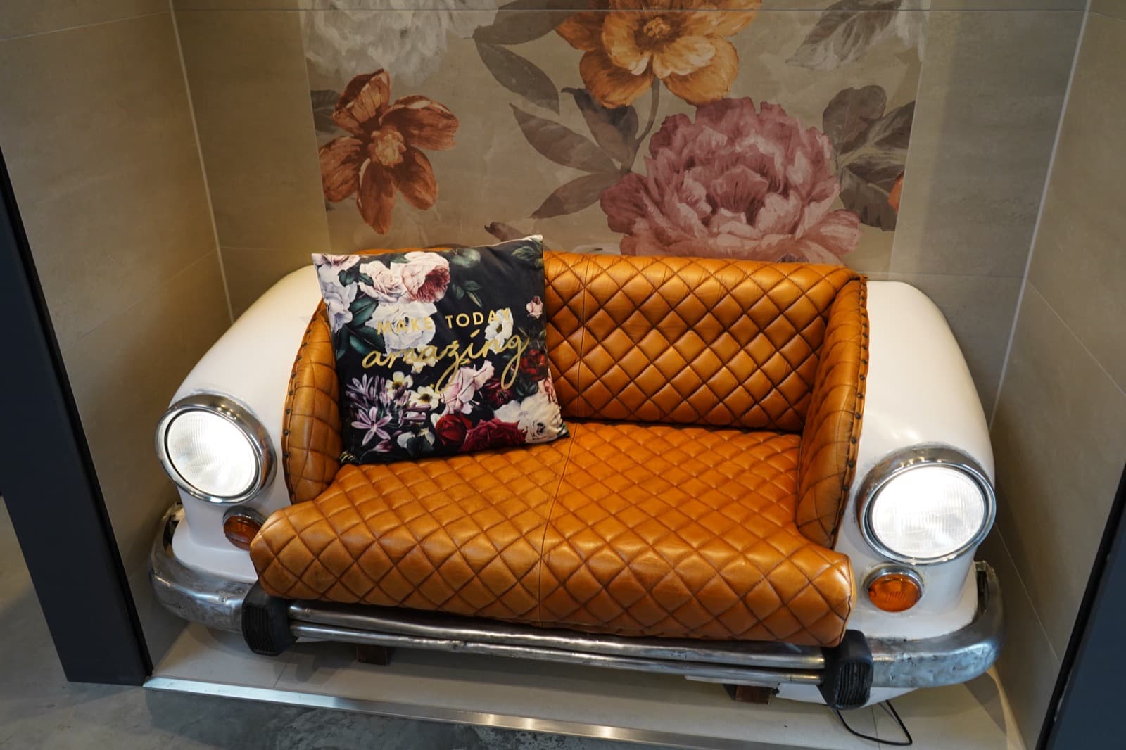 Sitznische in der Ausstellung: Ledersofa aus einer Oldtimer-Front mit Blumenkissen vor einem Rosen-Fliesenbild