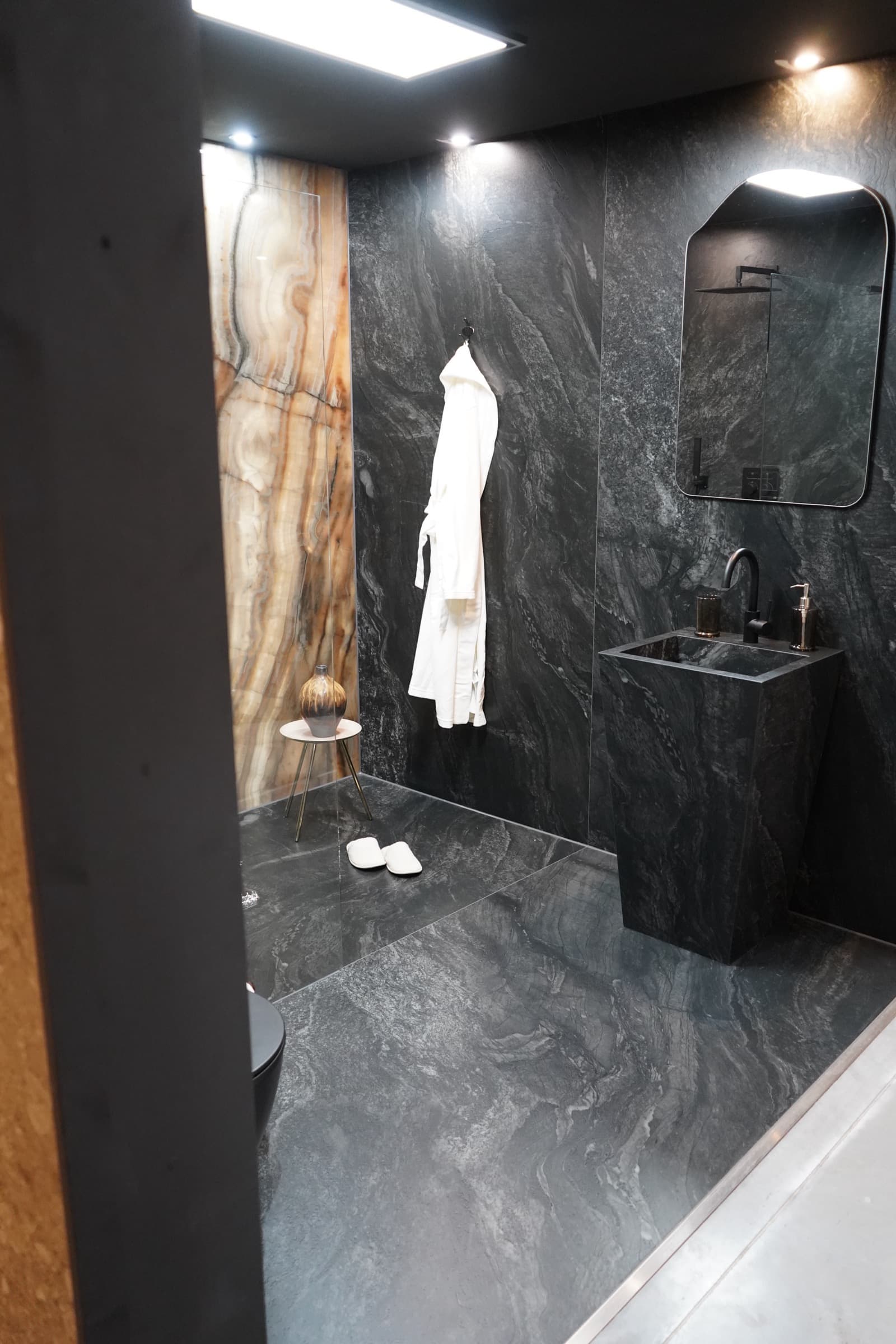 Dunkler Spa-Bereich der Ausstellung mit Standwaschtisch in Marmoroptik, Bademantel und hinterleuchteter Onyxwand