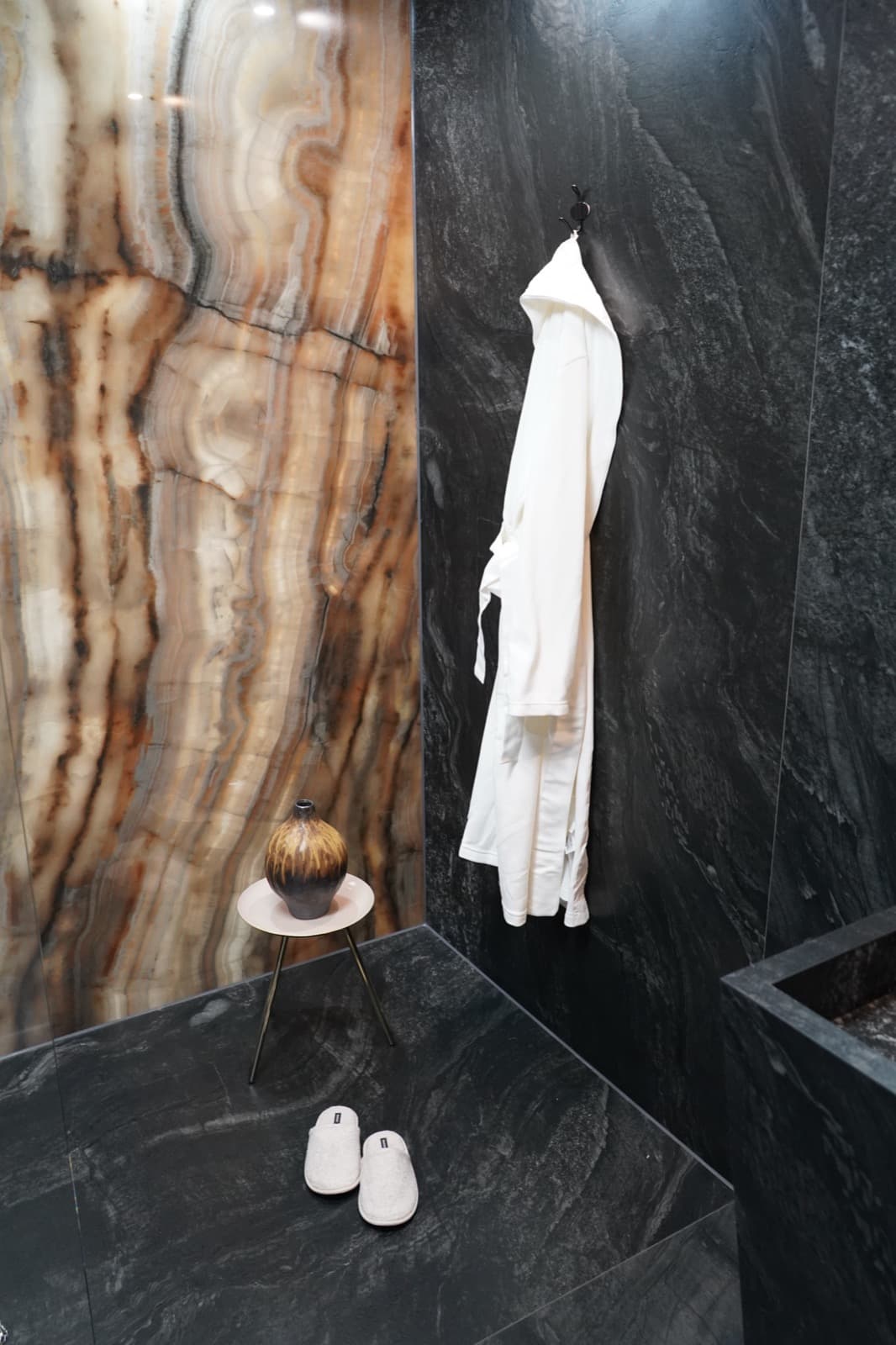 Dunkle Natursteinwand mit Bademantel und hinterleuchteter Onyx-Wand, Ausstellung von Greiner Fliesen